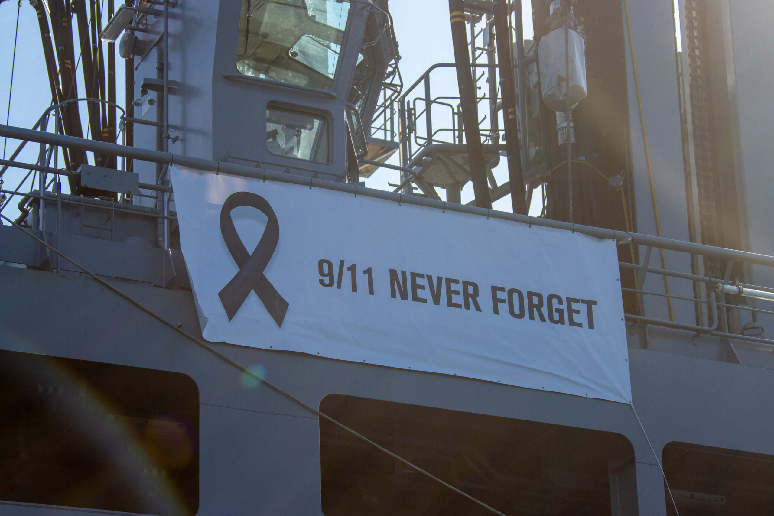 Banner mit der Aufschrift „9/11 Never Forget“ und schwarzer Schleife an einem Marineschiff. Das Bild erinnert an die Terroranschläge vom 11. September 2001.