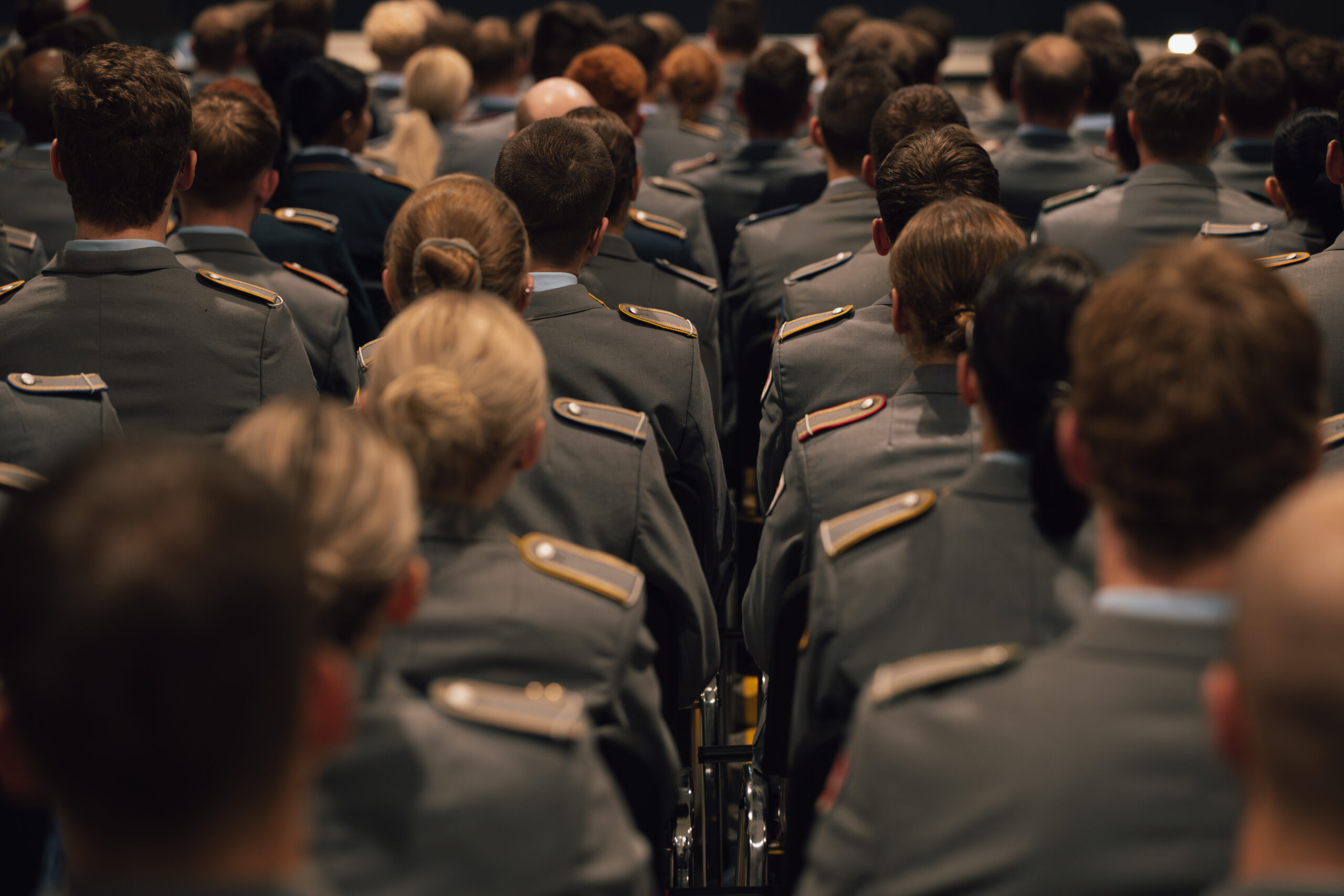 Mehrere Reihen von Studierenden in Uniform sitzen um den Roten Platz und verfolgen die Immatrikulationsfeier der HSU/UniBw H. Die Aufnahme zeigt das Publikum von hinten.