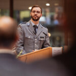Eine Person in Uniform spricht an einem Rednerpult der HSU/UniBw H vor den Gästen der Immatrikulationsfeier.