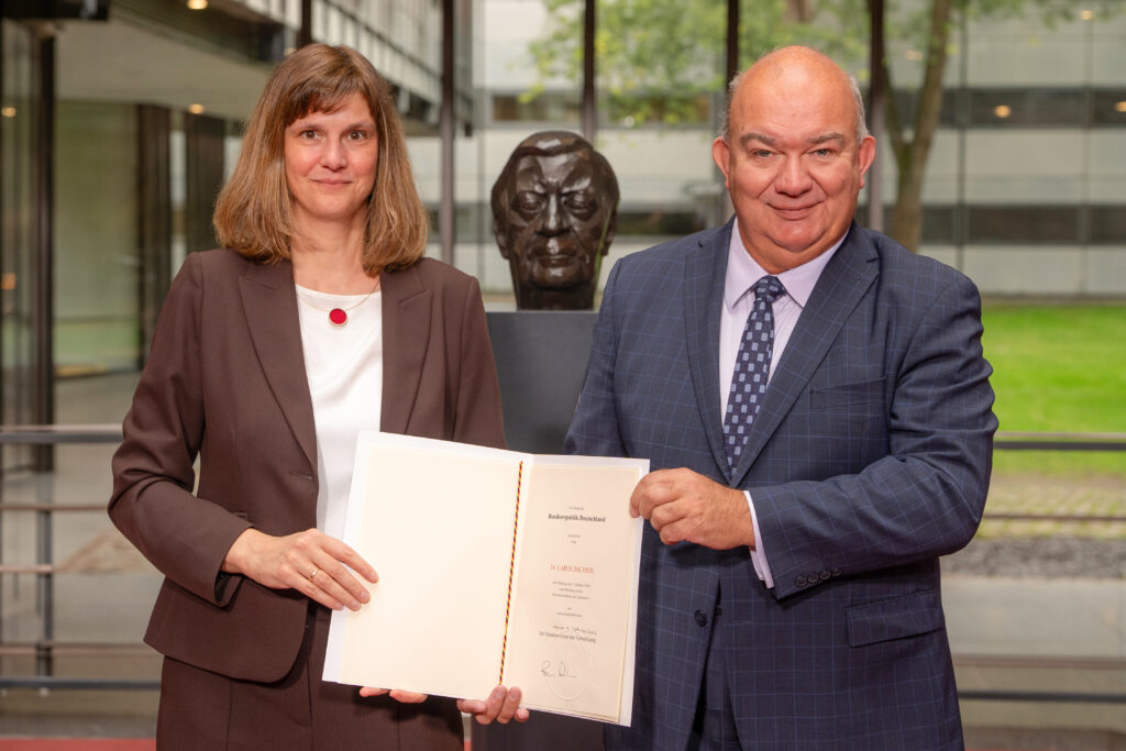 Zwei Personen stehen vor einem Roll-up der Helmut-Schmidt-Universität/Universität der Bundeswehr Hamburg und halten gemeinsam eine Ernennungsurkunde.